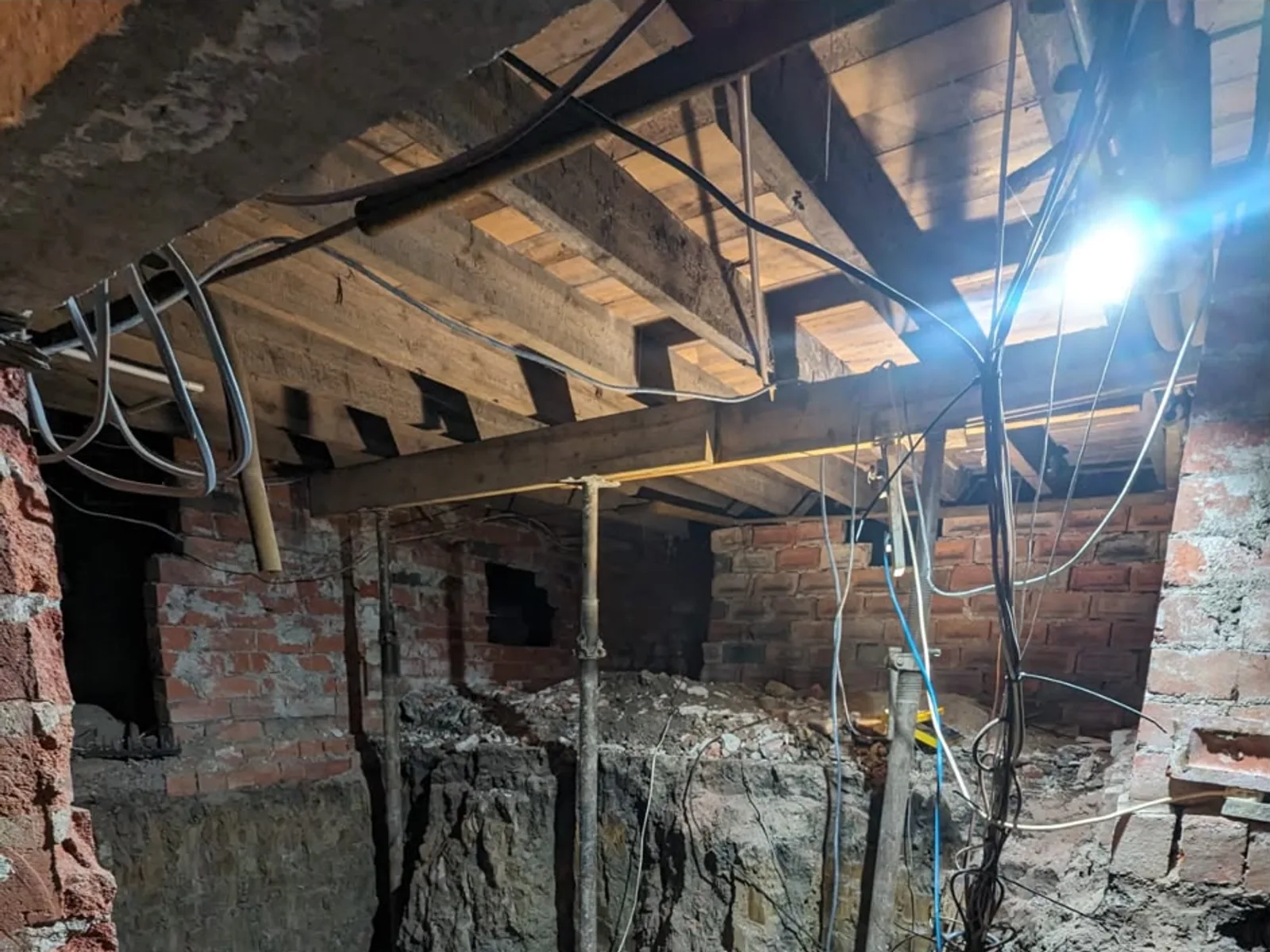 Victorian cellar mid-conversion with exposed joists, acrow props and dug-out floor before waterproofing