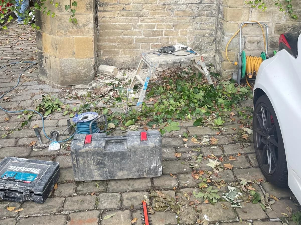 Halifax property exterior before groundworks, with overgrown stone yard and building materials