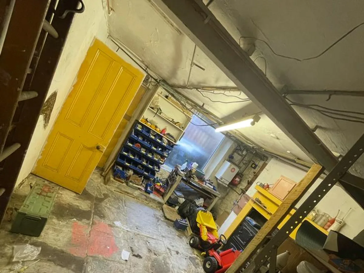 Cluttered Shipley cellar used for storage with shelving and a painted timber door before conversion